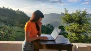 Frau arbeitet konzentriert am Laptop an einem Holztisch auf einer Terrasse mit Blick auf bewaldete Berge, Symbolbild für die 4-Tage-Woche und freie Zeiteinteilung