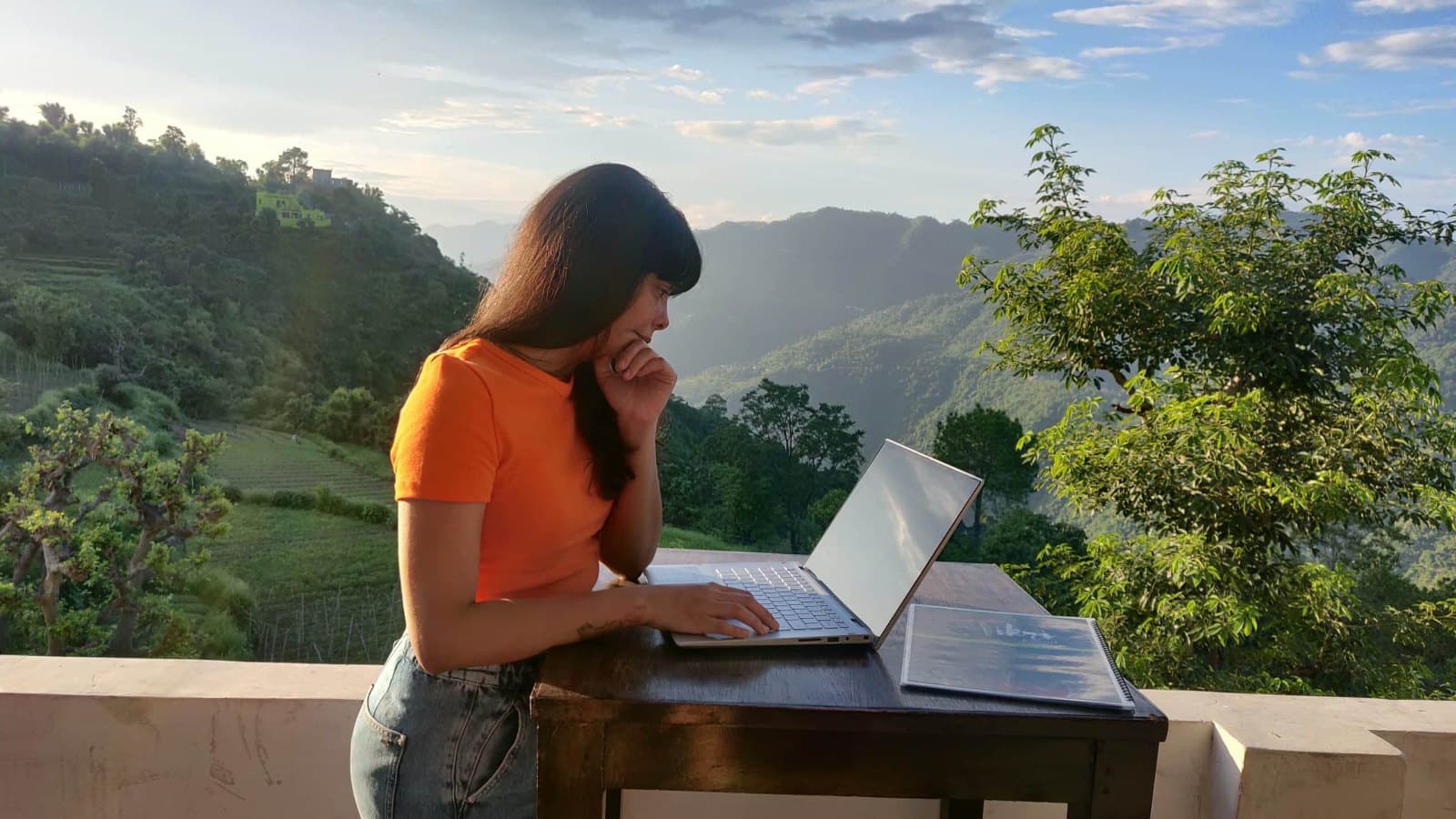 Frau arbeitet konzentriert am Laptop an einem Holztisch auf einer Terrasse mit Blick auf bewaldete Berge, Symbolbild für die 4-Tage-Woche und freie Zeiteinteilung